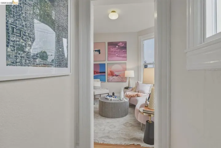 Open doorway revealing a brightly lit interior space with a bay window, light wood-finish flooring, and a flush mount ceiling light fixture