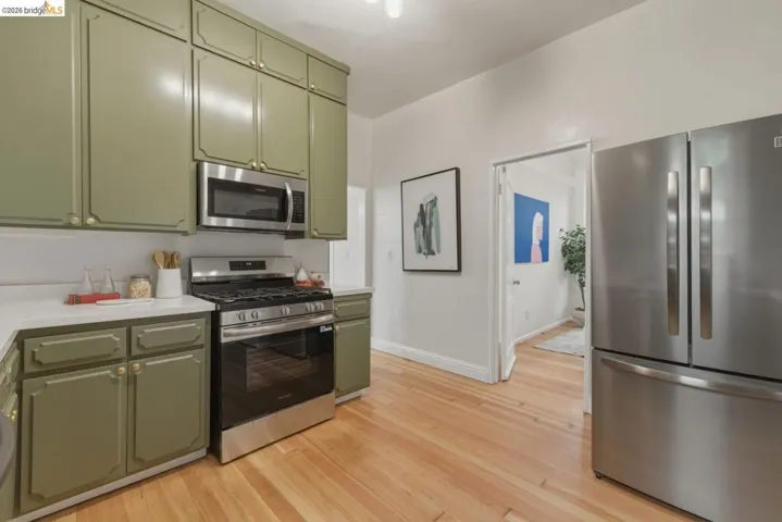 Kitchen featuring olive green cabinetry with gold hardware, stainless steel appliances, white countertops, and wood-finish flooring