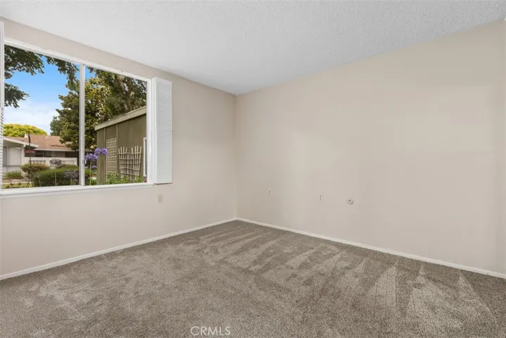 The secondary bedroom is bright and comfortable, offering large windows, plush carpeting, and flexible space for guests or a home office.