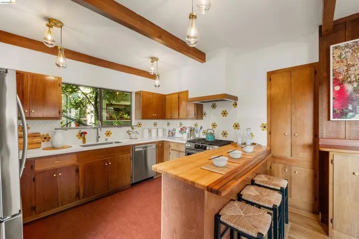 Kitchen featuring wood cabinetry, stainless steel appliances, a breakfast bar, exposed wood beams, and pendant lighting