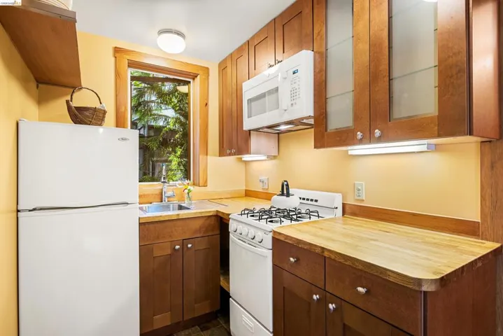 Compact kitchen featuring wood-finish cabinetry, light wood countertops, and a window above the sink