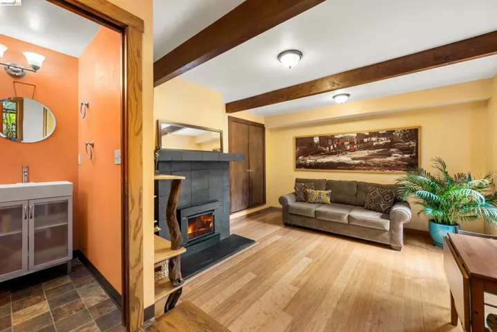 Living area with exposed beam ceiling, light wood-finish flooring, and a slate-tiled fireplace with an insert