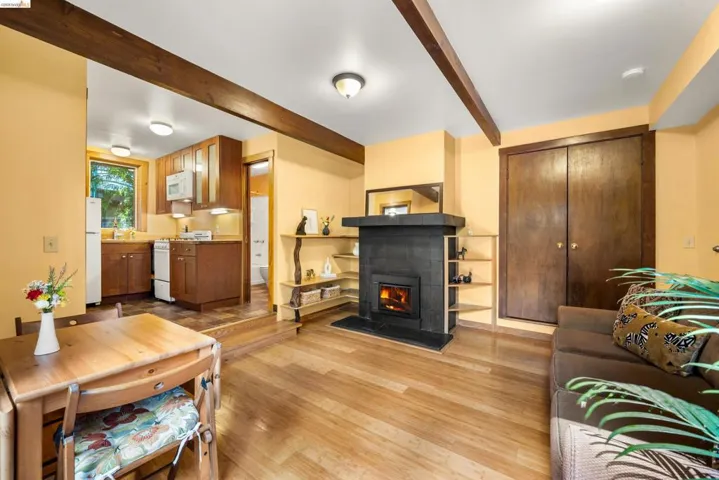 Living area featuring wood-finish flooring, exposed wooden ceiling beams, and a fireplace with a dark tile surround