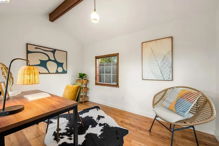 Vaulted ceiling with exposed wood beam, wood-finish flooring, and a window featuring a wood frame