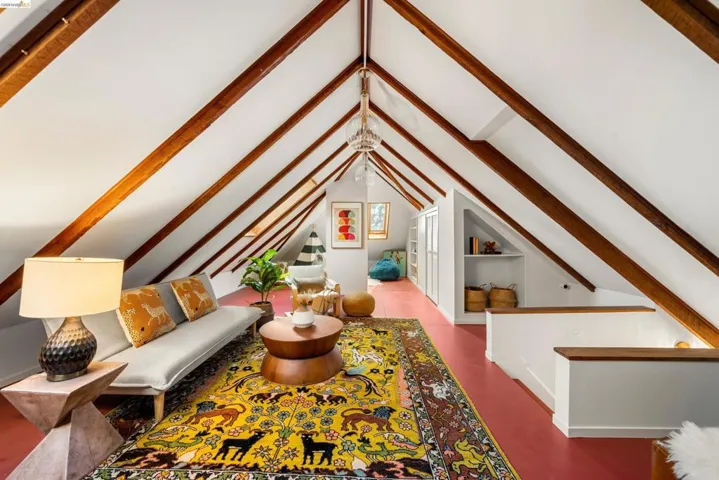 Vaulted ceilings with exposed wood beams, built-in shelving, white painted walls, and wood-finish flooring