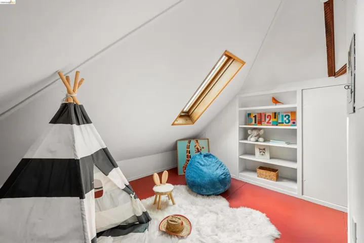 Attic space featuring an angled ceiling, a wood-framed skylight, built-in shelving, and a built-in storage cabinet