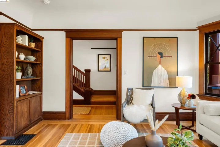 Living area featuring hardwood flooring, built-in shelving, rich wood trim throughout, and a doorway leading to a staircase