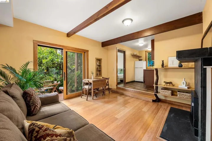 Living area featuring wood-finish flooring, exposed ceiling beams, and a black stone fireplace surround