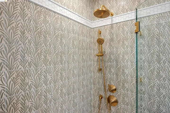 Shower enclosure featuring botanical-patterned wall tile, brushed gold shower fixtures, and a glass shower panel