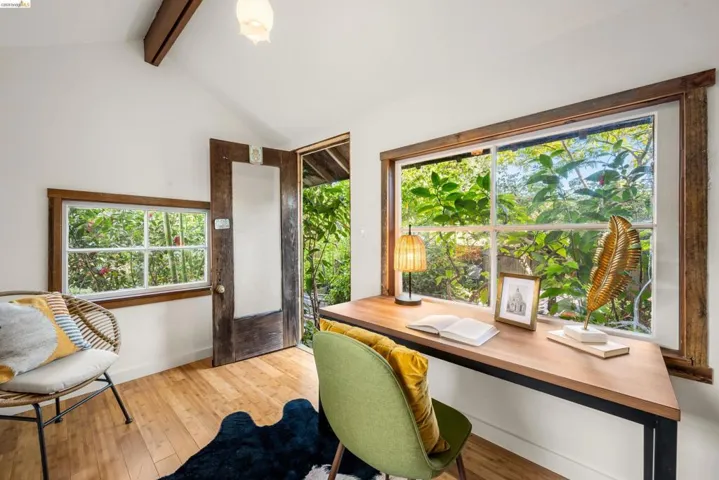 Vaulted ceiling with exposed wood beams, hardwood-finish flooring, and multiple windows with wood trim