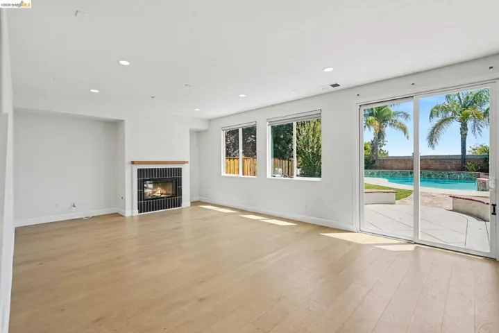 Spacious room featuring wood-finish flooring, a modern fireplace with a wood mantle and dark tiled surround, recessed lighting, and large windows