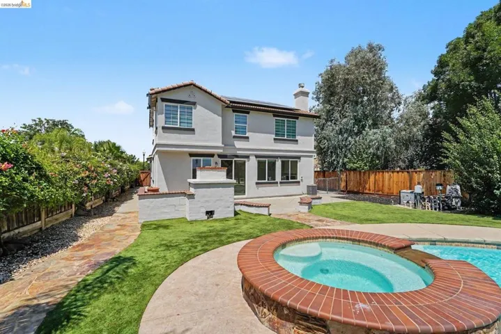 Backyard featuring a built-in spa with brick coping, a swimming pool, and a stucco exterior with multiple windows