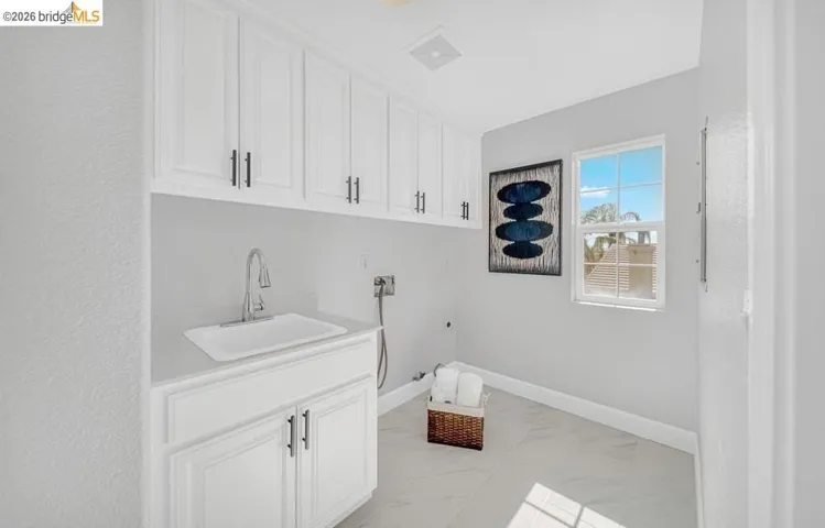 Laundry room featuring white cabinetry, a utility sink with a chrome faucet, light gray walls, and large format floor tiles