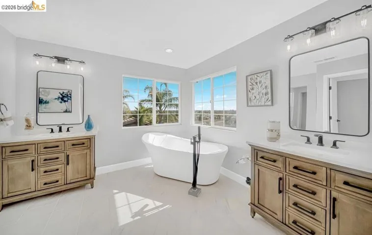 Freestanding soaking tub with a floor-mounted faucet, flanked by two separate wood-finish vanities with rectangular sinks and dark hardware