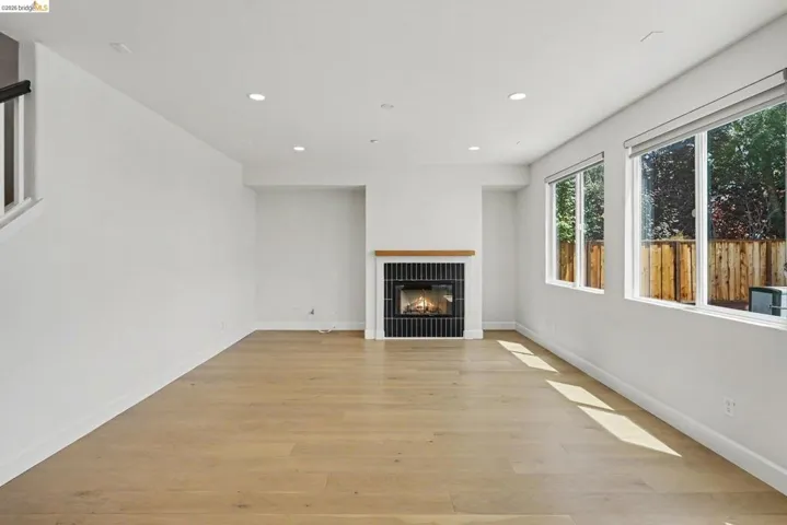 Spacious living area featuring light wood-finish flooring, a contemporary fireplace with black tile surround and wood mantel, multiple large windows, recessed lighting, and white baseboards
