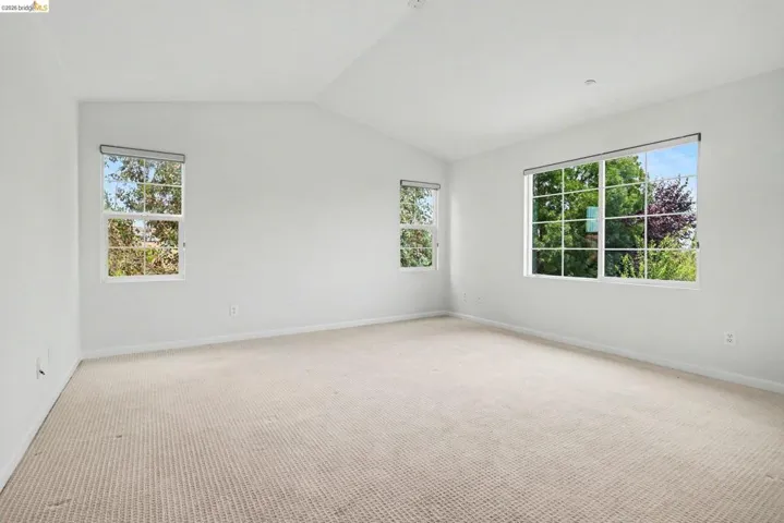Spacious room featuring vaulted ceilings, light-toned carpeting, and multiple windows providing abundant illumination