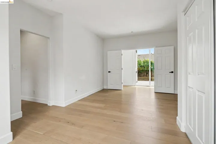 Spacious room featuring light wood-finish flooring, white walls, and bright white baseboards
