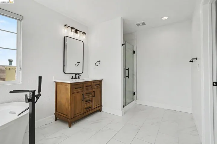 Bathroom featuring a freestanding tub with floor-mounted faucet, a wood-finish vanity with a white countertop and rectangular sink, a frameless mirror, and a glass-enclosed shower
