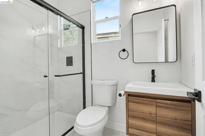 Sleek bathroom featuring a glass-enclosed shower with black trim, a wood-finish vanity with an integrated sink, a rectangular framed mirror, and matte black fixtures throughout