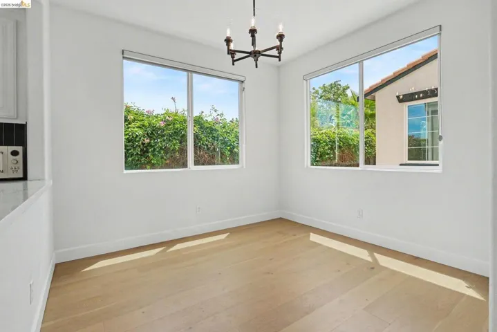 Bright room featuring two large windows, wood-finish flooring, a contemporary chandelier, and crisp white walls