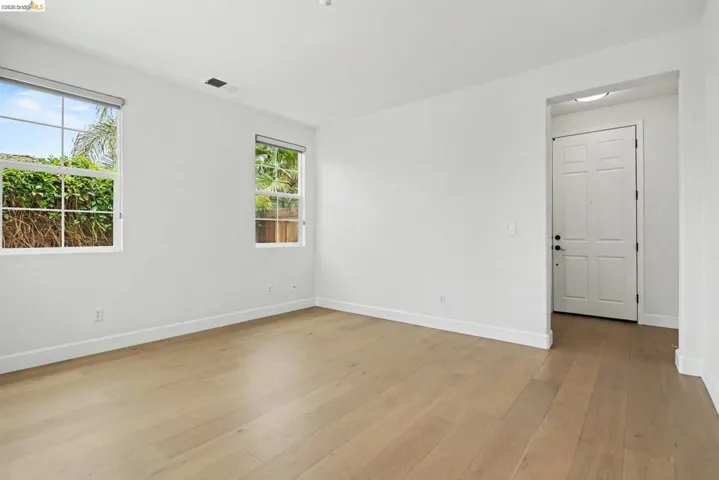 Bright room with wood-finish flooring, two large windows, white trim, and a paneled entry door