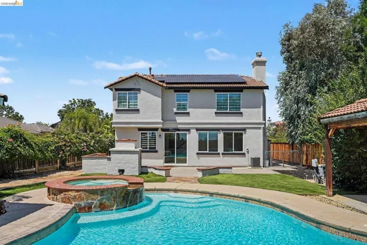 Rear exterior featuring a multi-level stucco facade, tile roof with solar panels, and a prominent chimney