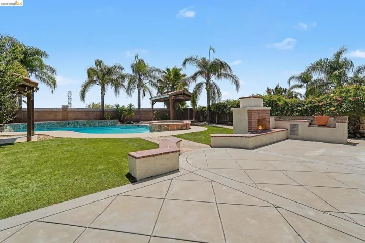 Expansive backyard featuring a concrete patio, built-in brick fireplace, and a swimming pool with a stone waterfall