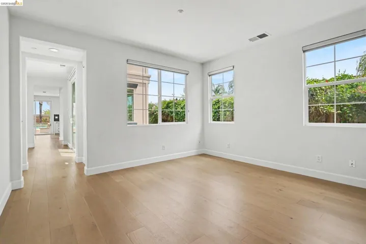 Bright interior room featuring wood-finish flooring, white baseboards, and multiple windows with roller shades