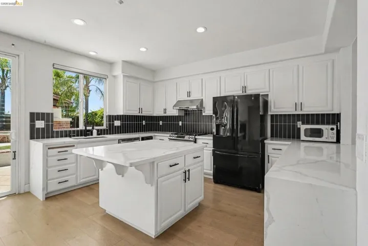 Modern kitchen featuring white cabinetry with dark hardware, a central island with a waterfall edge countertop, and a black tile backsplash