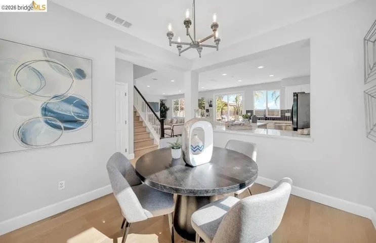 Dining area featuring light wood-finish flooring, a contemporary chandelier, a built-in kitchen pass-through, a staircase with dark handrails, and recessed lighting