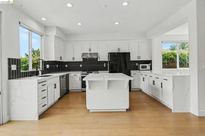 Contemporary kitchen with white cabinetry, black linear tile backsplash, and light wood-finish flooring