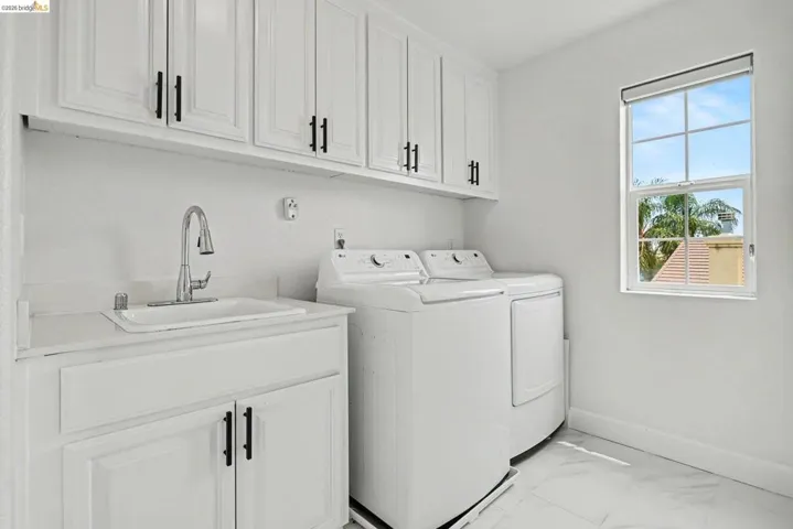 Laundry room featuring upper and lower cabinetry with black hardware, a utility sink with a chrome gooseneck faucet, and a window with natural light