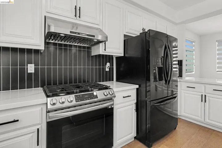 Kitchen featuring white cabinetry with matte black hardware, a stainless steel range with overhead ventilation, a black French-door refrigerator, and wood-finish flooring
