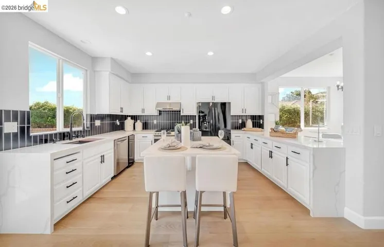 Spacious kitchen featuring an extended center island, white cabinetry, integrated stainless steel appliances, light wood-finish flooring, and a dark tile backsplash