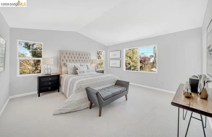 Vaulted ceilings highlight this room featuring light-colored carpeting and multiple windows