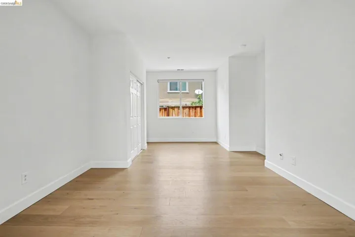 Spacious room featuring wood-finish flooring, white walls, and a large window providing natural light
