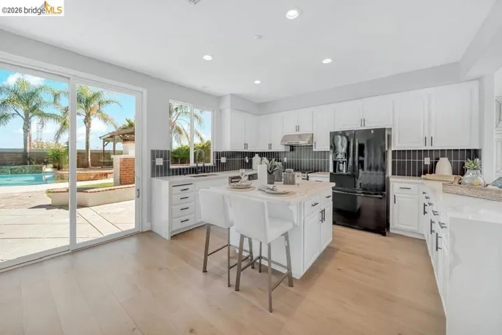 Open-concept kitchen featuring wood-finish flooring, white cabinetry, a central island with countertop seating, and a black appliance package