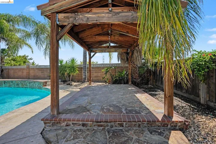 Wood pergola structure with a stone tile floor, brick base, and integrated lighting