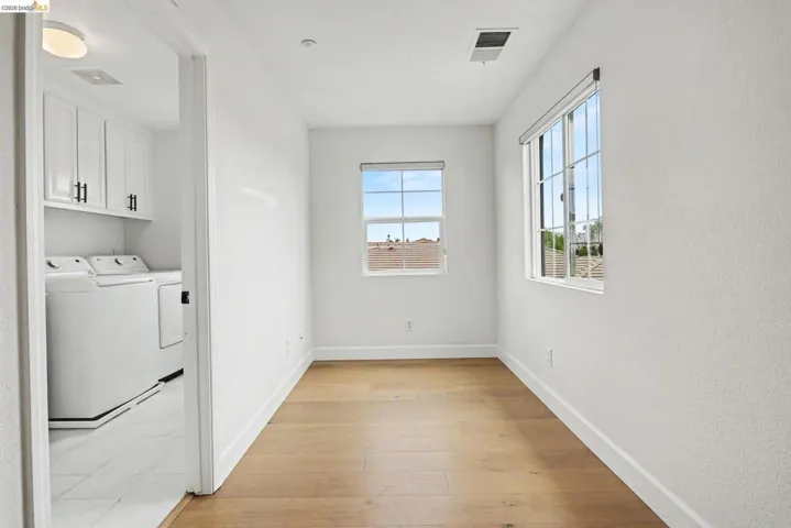 Bright room featuring wood-finish flooring, two windows with blinds, and white baseboards