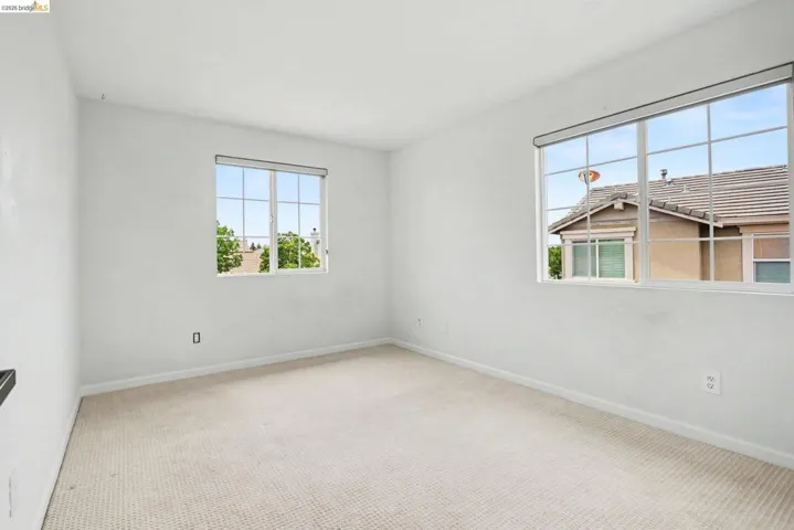 Neutral color palette room featuring two multi-pane windows, light-toned carpeting, and white baseboards