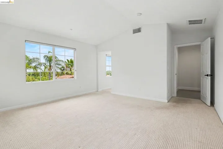 Carpeted interior space featuring a large multi-pane window, vaulted ceiling, and recessed lighting