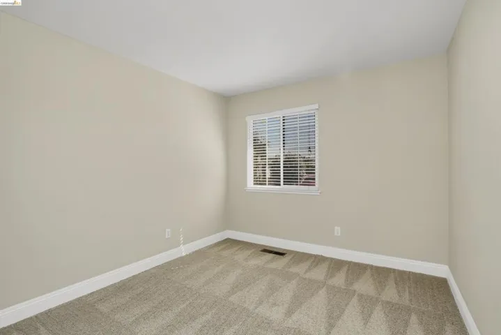 Neutral wall color, white trim, window with blinds, light-colored patterned carpeting, and a ceiling-mounted light fixture