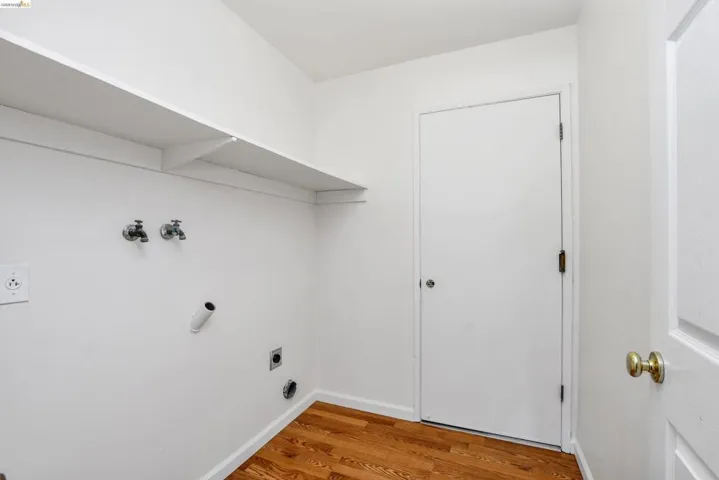 Laundry area featuring wood-finish flooring, white walls, and an integrated shelf for storage