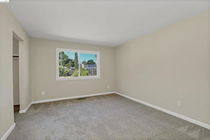 Light-filled room featuring neutral wall paint, gray carpet flooring, white baseboards, and a window with white trim