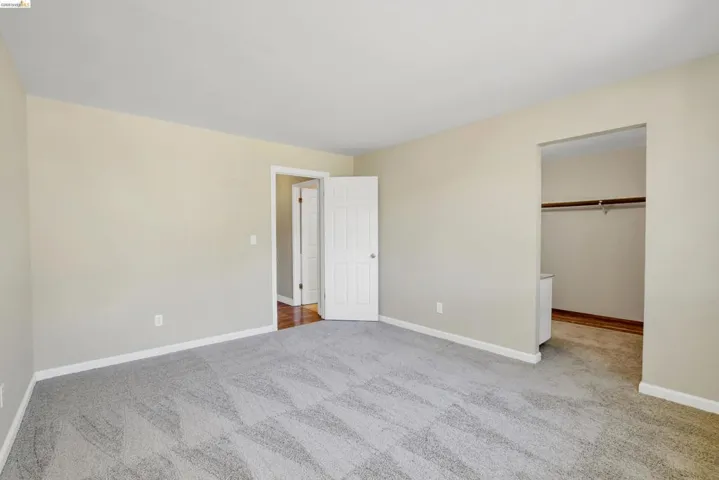 Spacious room featuring light neutral wall paint, white trim, and patterned gray carpeting