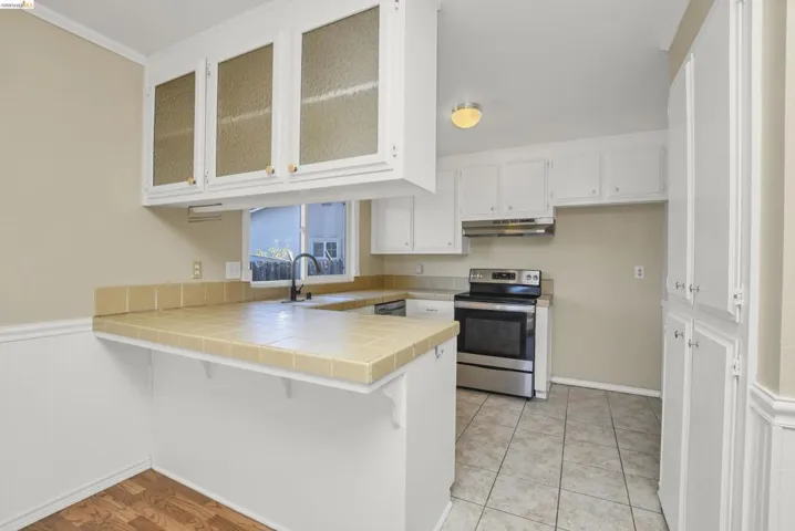 Kitchen featuring white cabinetry, tile countertops, stainless steel range, and tile flooring