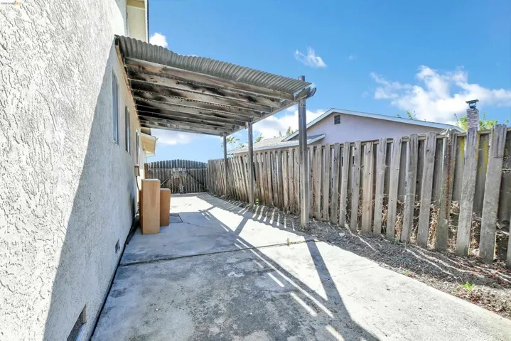 Side yard featuring a concrete pathway, a corrugated metal awning, and a privacy fence