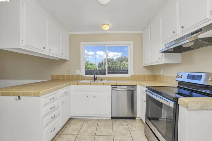 U-shaped kitchen featuring white cabinetry, tile countertops, tile flooring, stainless steel appliances, and a window above the sink