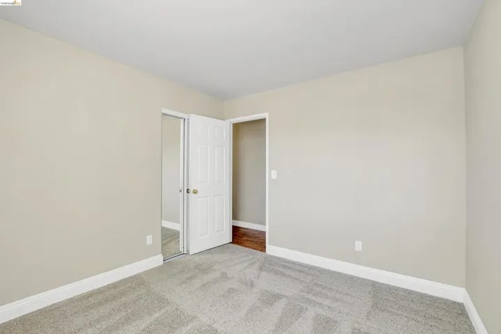 Room featuring neutral wall tones, light gray carpet, white baseboards, and a mirrored closet door