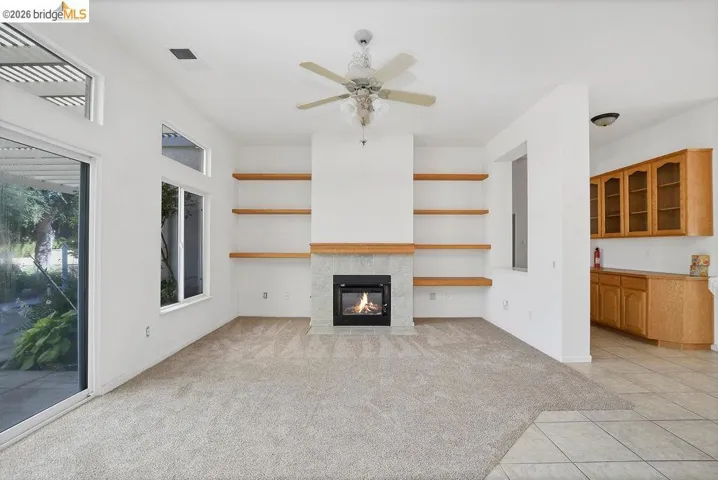 Living area featuring a fireplace with a light-colored stone surround and wood mantle, built-in open shelving, and a ceiling fan